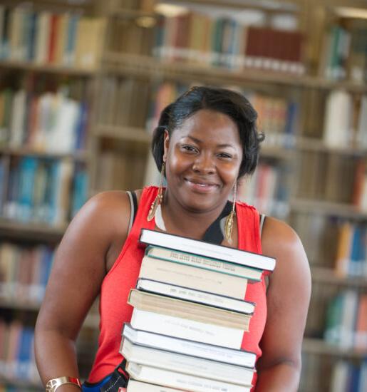 Woman in library holding a stack of books.